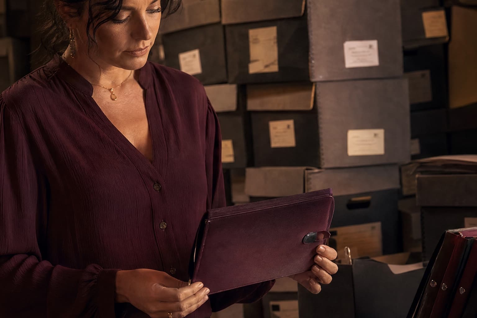 Adult reader choosing an organized travel binder beside overflowing archive boxes